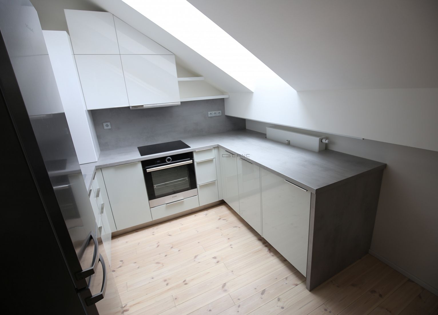 Moderní rohová kuchyň na míru s bílým leskem a betonovými prvky.