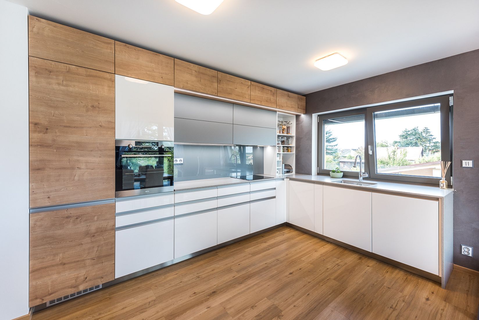 Moderní kuchyň ve tvaru "L" s bílými lakovanými skříňkami a moderními prvky